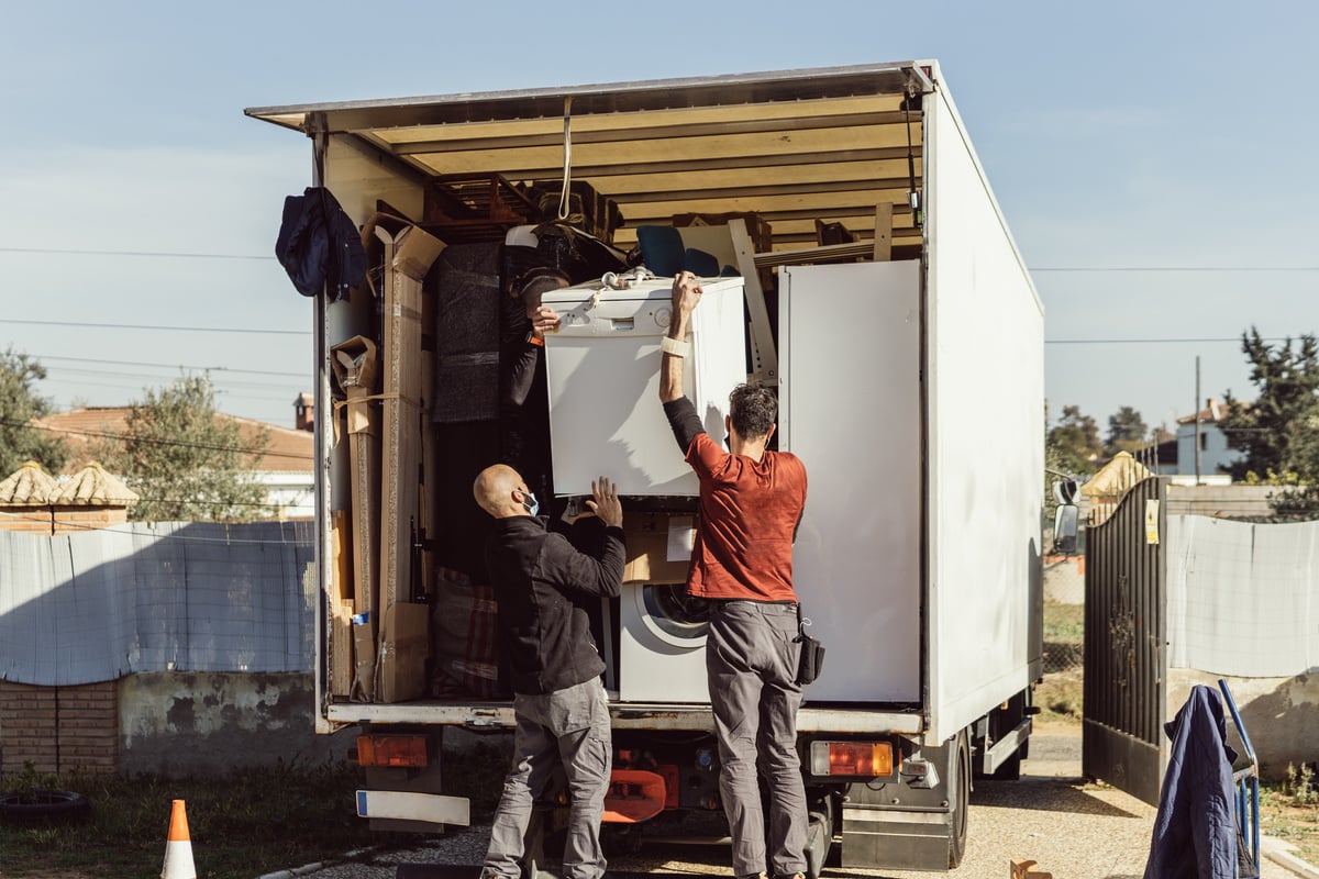 3 colleagues of a moving company load a dishwasher onto the